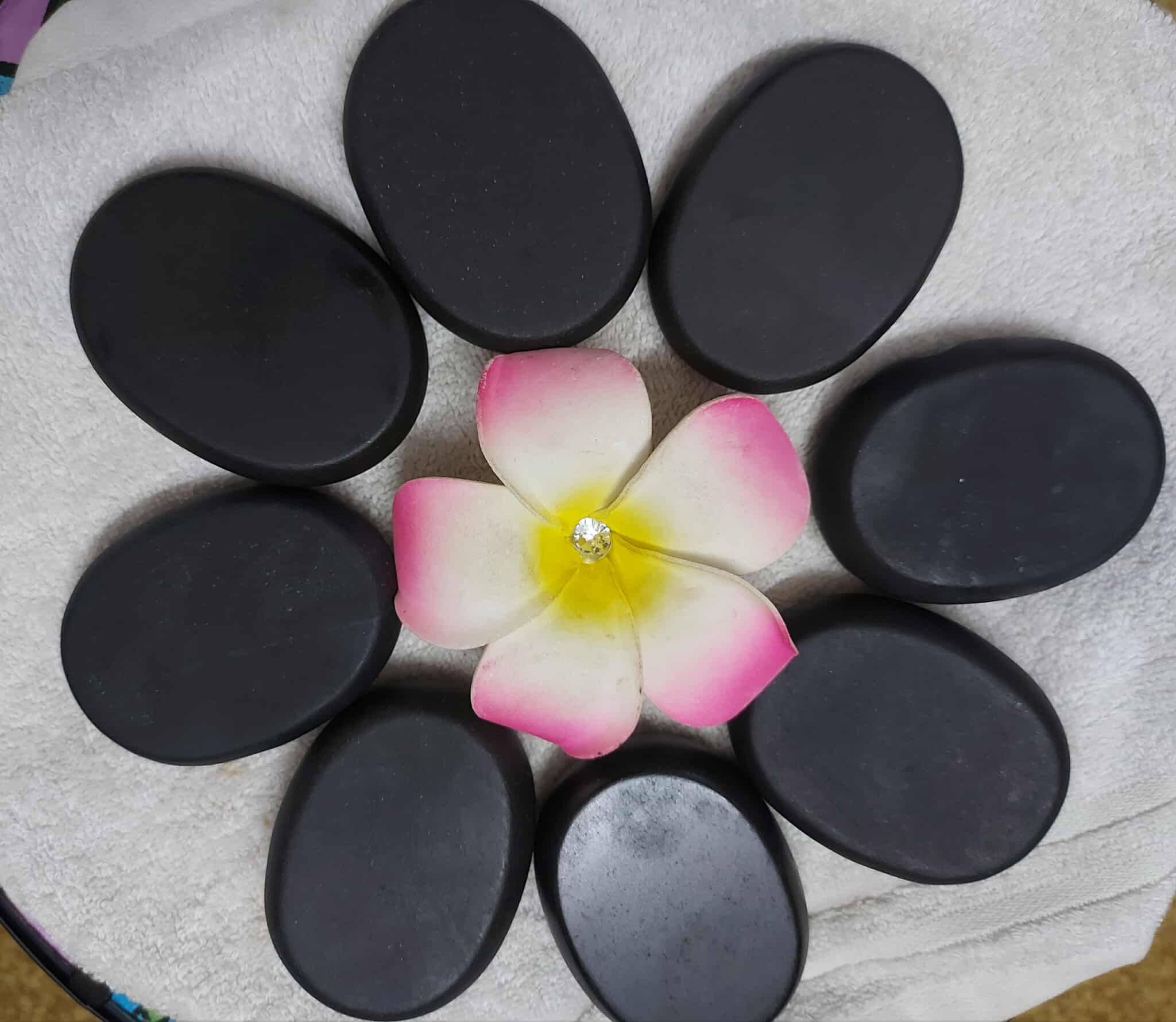 Basalt hot stones laid out in a flower shape around a frangipani on a white towel